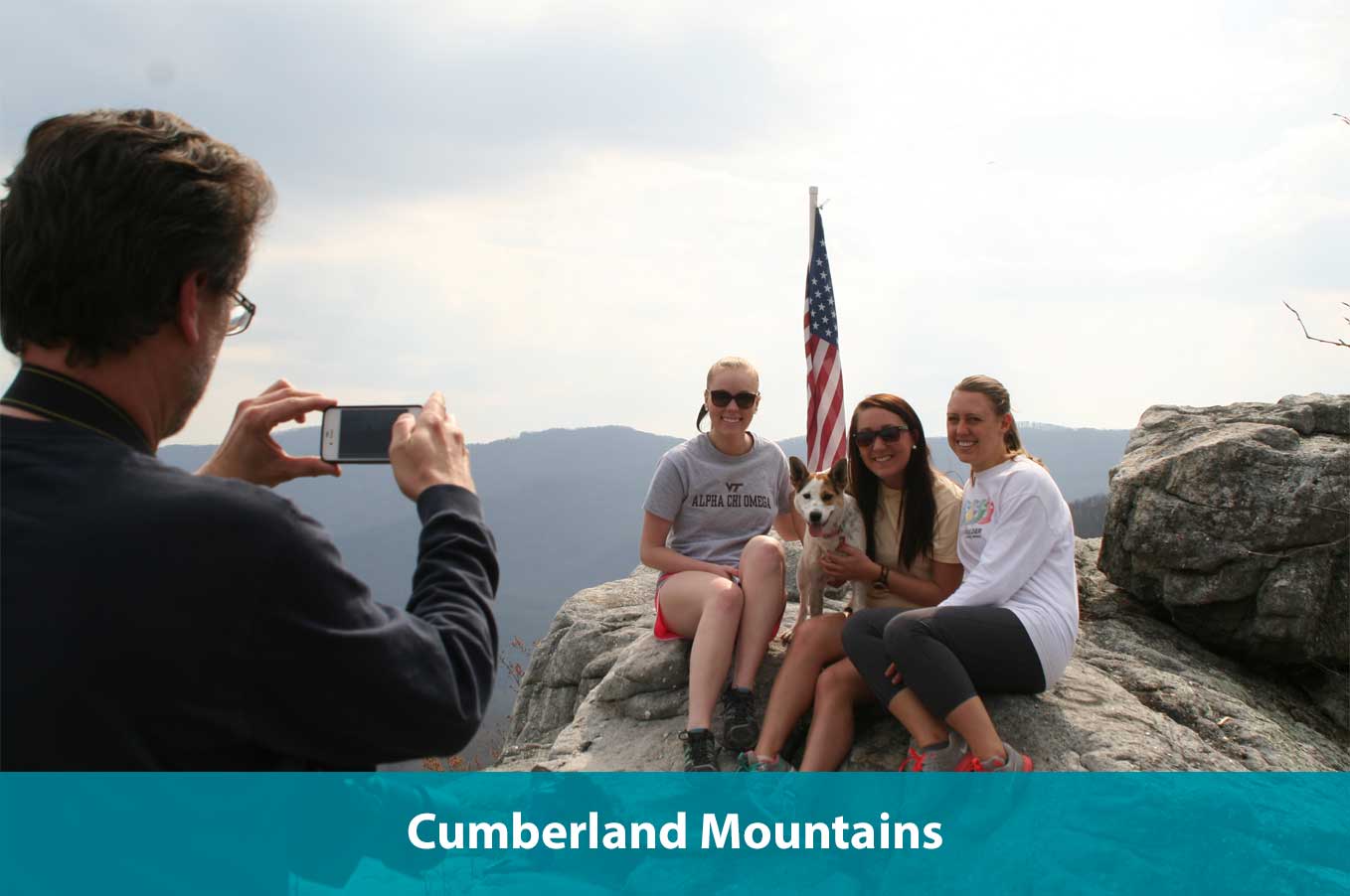 Father taking picture of family sitting on rock with dog with Cumberland Mountains in background